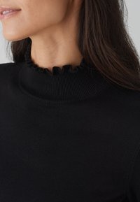 Schwarzer Strickpullover mit einem gerafften Ausschnitt, gerippter Textur und figurbetontem Design. Nahaufnahme des Kragens.