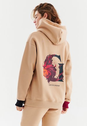 Béžová mikina s kapucňou s veľkým emblémom Gryffindoru so levom a písmenom 'G' na chrbte. Bavlnený materiál s kontrastnými manžetami na rukávoch.