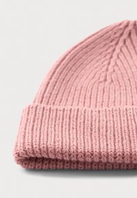 Cappello beanie rosa lavorato a maglia, piegato, con motivo a coste e risvolto su una superficie bianca.