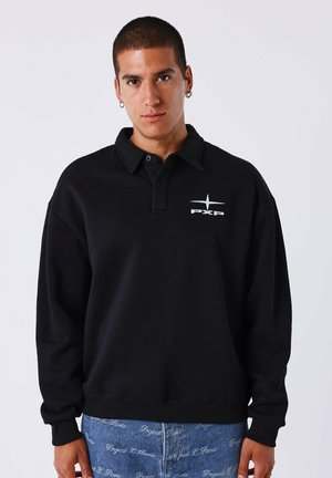 Sweatshirt noir à col et patte de boutonnage, arborant un logo PXP blanc sur la poitrine, assorti avec un pantalon en denim.