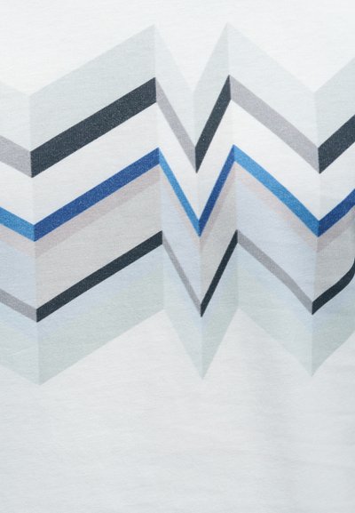 Κοντομάνικο μπλουζάκι με γεωμετρικό μοτίβο που παρουσιάζει διαπλεκόμενα ζιγκ-ζαγκ σε αποχρώσεις του μπλε, γκρι, μαύρου και λευκού σε ανοιχτό φόντο.