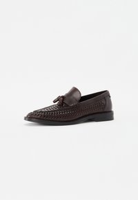 Brune læderslippers med et vævet design over forpartiet, en afrundet tå og en lille kvastdetalje foran. Flad sål.
