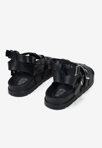 Sandalias negras con múltiples correas y hebillas, hechas de material suave. Suela gruesa y diseño plano con plantilla texturizada.