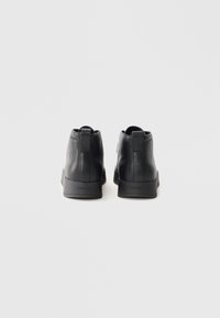 Une paire de bottines noires en cuir avec une surface texturée et le logo Calvin Klein à l'arrière de la semelle, vue de derrière.