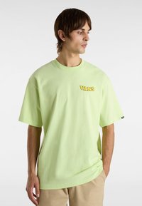 Light green cotton t-shirt with short sleeves, featuring a yellow "VANS" logo on the left chest area. Relaxed fit with a round neckline.