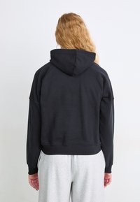 Sudadera negra recortada con capucha, mangas raglán y puños acanalados. Combinada con pantalones de chándal grises claros, mostrando un ajuste relajado.