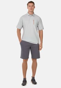 Polo shirt grigio chiaro con taschino e zip arancione, abbinato a pantaloni corti grigio scuro e scarpe da ginnastica grigie.