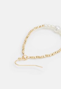 Auksiniai karoliukų auskarai su mažais apvaliais karoliukais ir dideliu baltu perlu; turi kabliuko formos užsegimą. Lygus ir blizgus paviršius.