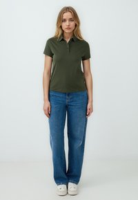 Polo shirt verde scuro con colletto e tre bottoni. Abbinato a jeans di denim blu Larghi e sneakers bianche.