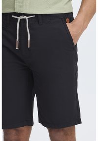 Svarte shorts laget av slitesterkt stoff med snøring i livet. Har lommer og et lærlogoakkent på midjebåndet.