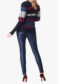 Suéter de rayas en navy, gris, rojo y teal; textura acanalada. Pantalones navy de tiro alto ajustados; acabado brillante. Calzado con tacones rojos que complementa.
