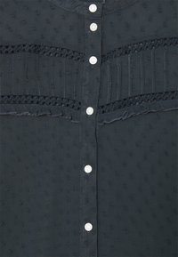 Camicia blu scura con bottoni in tessuto testurizzato, caratterizzata da piccoli motivi alternativi e dettagli in pizzo, rifinita con chiusure a bottoni bianchi.