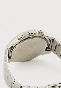 Ezüst Tommy Hilfiger fém karóra hátulja, három texturált állító koronával és láncos karkötős zenekarral.