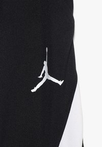 Černé sportovní oblečení s texturovaným designem a výrazným bílým logem Jumpman. Doplňováno kontrastním bílým panelem.