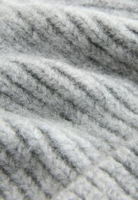 Tissu en tricot gris présentant un motif texturé avec des fibres visibles et des mailles douces et lâches, créant une apparence chaleureuse et confortable.
