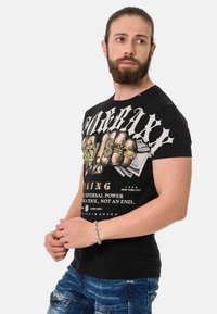 Schwarzes T-Shirt mit einem auffälligen weißen und goldenen Grafikdruck eines geballten Fists sowie Text, taillierte Passform, kurze Ärmel und aus Baumwollstoff.
