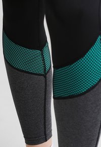 Černé a šedé legíny s tyrkysovými síťovinovými panely, s těsným střihem a plochými švy pro pohodlí a odolnost.