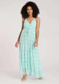 Maxiklänning i ljus mintgrön med blå diamantmönster, v-ringning, justerbara remmar och samlad midja, med en flödande flerlagerskjol.