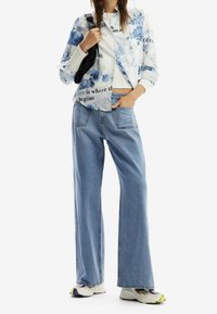 Blumenmusterhemd mit blauen Akzenten, kombiniert mit weiten, hellblauen Jeans und weißen Sneakers mit bunten Details.