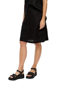 Jupe en lin noire avec une taille élastique et une poche latérale, assortie à des sandales noires à lanières avec une semelle épaisse.