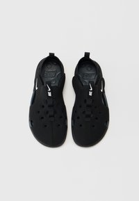 Czarne, lekkie buty na wsuwanie z dużymi otworami, teksturowaną podeszwą i przednim paskiem z białym logo Nike. Wnętrze z okrągłym wzorem.