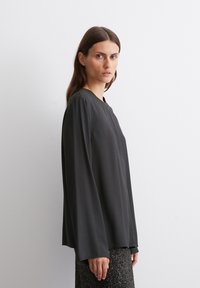 Black long-sleeve shirt with a round neckline, made from smooth fabric. Features relaxed fit and slightly flared sleeves.