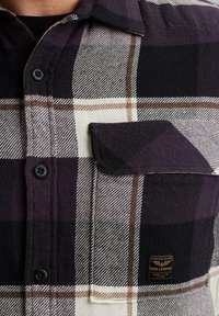 Karierte Flanellhemd in Schwarz, Weiß und Lila, ausgestattet mit einer Brusttasche, Knopfleiste und strukturiertem Stoff mit kontrastierenden Mustern.