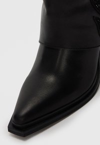 Black leather ankle boot with a pointed toe and smooth texture. Features a folded cuff design and a flat, rectangular sole.