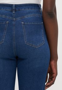 Mørkeblå skinny jeans har høy midje, fem-lommers design og kontrasterende sømdetaljer på baklommene.
