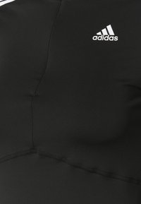 Czarna tkanina odzieży sportowej Adidas z widocznymi szwami i białym logo Adidas w górnym prawym rogu.