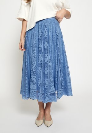 Jupe midi en dentelle bleue avec des motifs complexes et une taille ajustée, présentant un design plissé et un ourlet festonné. Portée avec des talons de couleur claire.