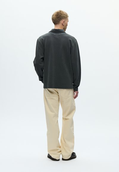 Παντελόνι μπεζ και oversize σκουρόχρωμο γκρι πουκάμισο με μακριά μανίκια και κολάρο. Μινιμαλιστικός σχεδιασμός και λεία υφή.