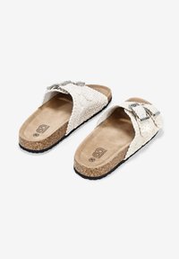 Sandalias deslizantes blancas trenzadas con dos hebillas ajustables de plata, plantilla de corcho y plantilla de tan texturizada. Suela de goma negra para agarre.