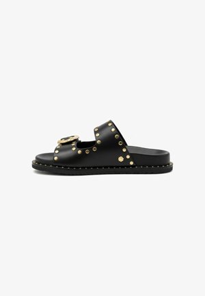 Sandalia negra tipo chancla con tachuelas doradas y detalle de hebilla en dos tiras, suela plana y diseño de punta abierta.