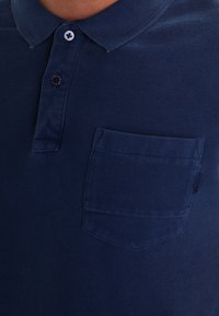 Navyblaue Poloshirt mit einem knöpfbaren Kragen, einer Brusttasche und strukturiertem Stoff mit kontrastierenden Knöpfen. Klassische Passform und minimalistisches Design.