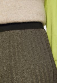 Maglione beige sovrapposto a una cintura elastica nera. Tessuto grigio scuro e strutturato con un motivo a spina di pesce sotto la vita.