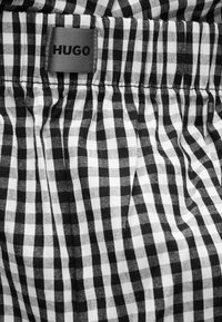 Tissu à carreaux noir et blanc avec taille froncée et une étiquette grise cousue portant l'inscription « HUGO » en lettres noires.