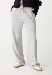 Lichtgrijze sweatpants van zachte stof, met een tailleband met trekkoord, zijzakken en een ontspannen, wijdvallende pasvorm. Gemaakt met witte sneakers.