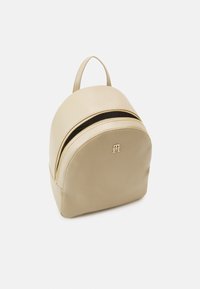 Zaino in pelle beige dalla forma arrotondata, con doppi zip dorati e una maniglia superiore. Presenta un logo impresso sul fronte.