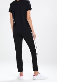 Camiseta negra de manga corta combinada con pantalones negros que tienen una franja lateral blanca, llevada con zapatillas blancas. Diseño simple y casual.