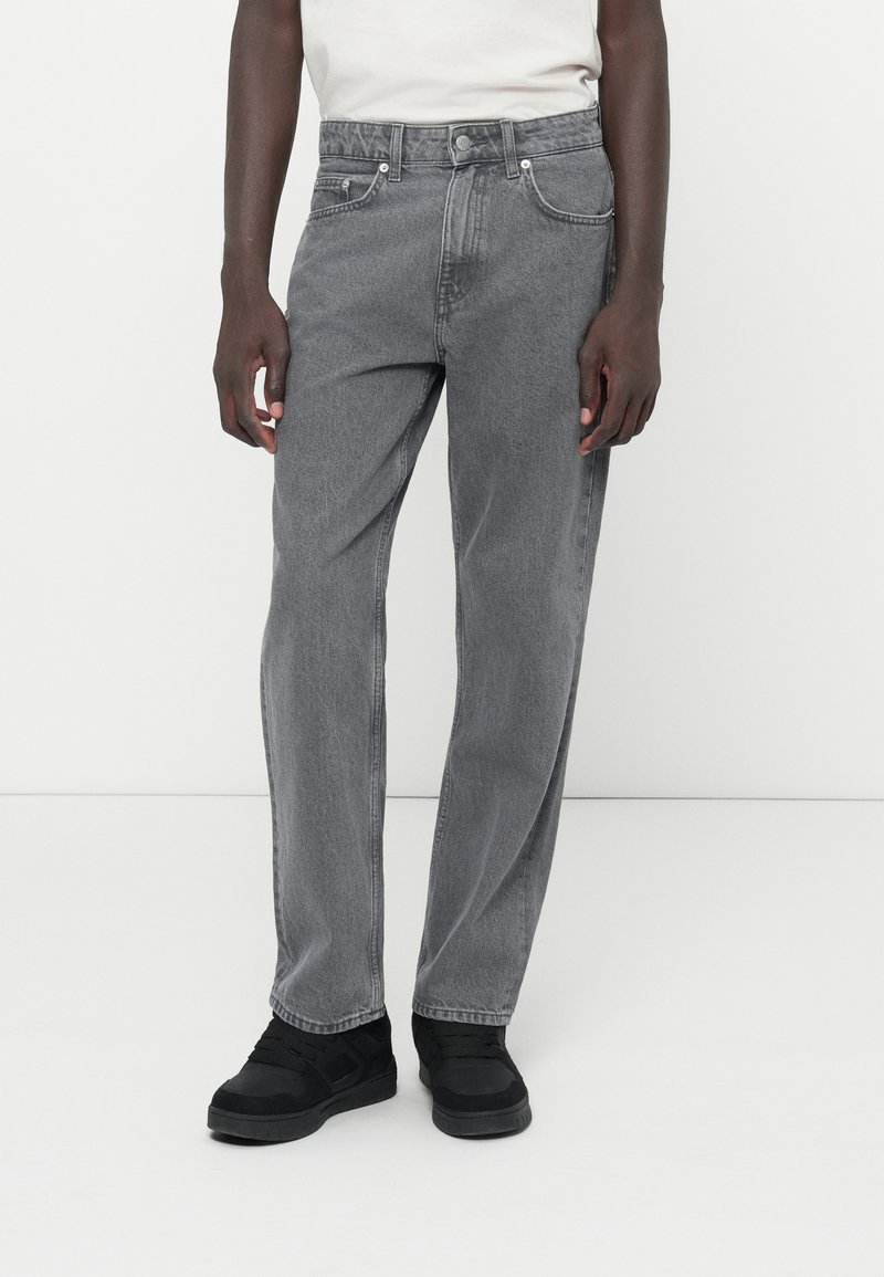 Jeans in denim grigio con taglio dritto, cinque tasche e cuciture sottili. Indossati con calzature nere, dotate di un colletto imbottito.