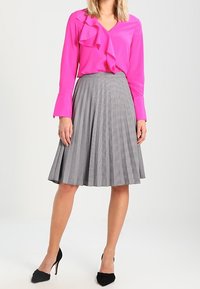 Fuchsiová blůza s volánkem a výstřihem do V, v kombinaci se šedou kostkovanou plisovanou sukní. Černé lodičky na vysokém podpatku dokončují vzhled.