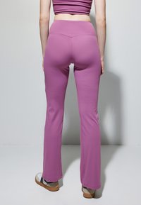Paarse flare leggings met een fits taille, een gladde textuur en minimale stikdetails. Draagt met lichtgekleurde schoeisel.