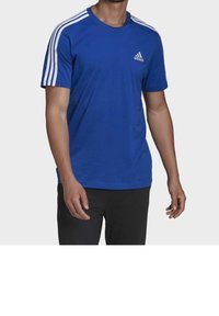 Blå Adidas t-shirt i bomull, med vita tre-stripesdetaljer på ärmarna och en liten logo på bröstet. Korta ärmar, rund halsringning.