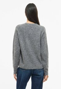 Suéter de lana gris con mangas largas, corte relajado, cuello redondo y acabado texturizado. Combinado con vaqueros azul oscuro, mostrando un estilo casual.