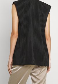 Svart randig ärmlös topp med axelvaddar, med en avslappnad passform och rak skärning. Matchad med ljusa satinbeiga byxor.