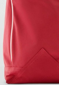 Tote en tissu rouge avec une texture lisse, présentant un accent triangulaire en bas et des coutures blanches contrastantes sur le côté.