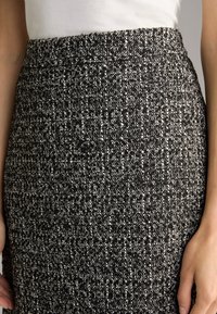 Zwart-witte tweed rok met een gestructureerd patroon, een gladde tailleband en een op maat gemaakte pasvorm. De stof heeft een geweven ontwerp met verschillende draaddiktes.
