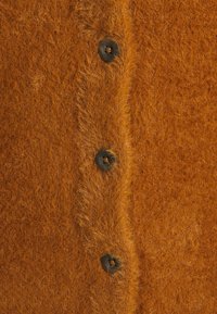 Orange stickad kofta med fluffig textur, med fem svarta knappar längs fram. Fokusera på de mjuka, upphöjda fibrerna.