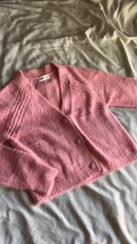 Rozā, pūkaina kardigāna ar V veida kakla izgriezumu, garām piedurknēm un trim pogām. Mīksta tekstūra ar ribotu detaļu gar pleciem un aprocēm.